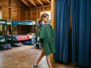 Tween camper in a cabin using a big t-shirt or robe for privacy while heading to change.